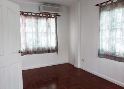 Empty room with wooden floor, two windows with curtains, and an air conditioning unit