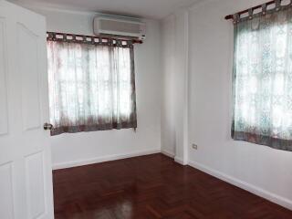 Empty room with wooden floor, two windows with curtains, and an air conditioning unit