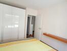 Well-lit bedroom with wardrobe and wall-mounted shelf