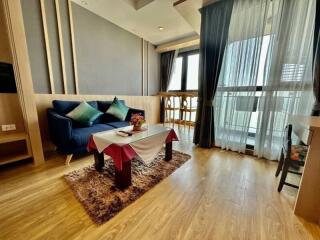 Modern living room with hardwood floors, a blue sofa, coffee table, large windows, and balcony.