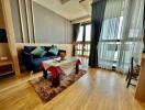 Modern living room with hardwood floors, a blue sofa, coffee table, large windows, and balcony.