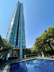 Tall modern residential building with a pool and surrounding greenery