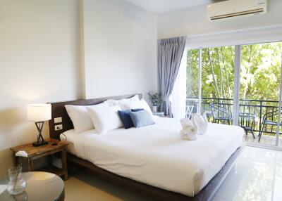 Spacious bedroom with a large bed, bedside table, lamp, and sliding glass doors leading to a balcony