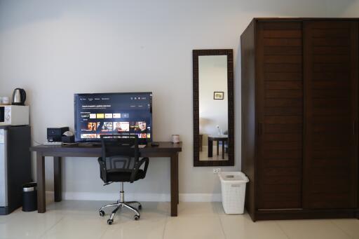 A bedroom with a TV on a desk, chair, wardrobe, mirror, and laundry basket