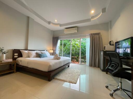 Spacious modern bedroom with large bed and workstation next to a window with garden view