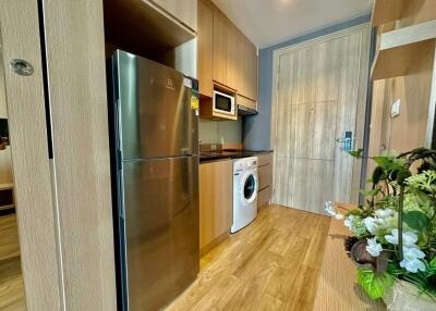Modern kitchen with wooden cabinetry, stainless steel fridge, washing machine, and built-in microwave