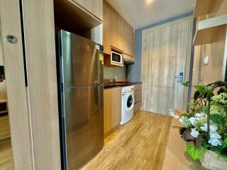 Modern kitchen with wooden cabinetry, stainless steel fridge, washing machine, and built-in microwave