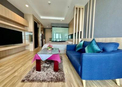 Modern living room with blue sofa, coffee table, TV, and view of bedroom