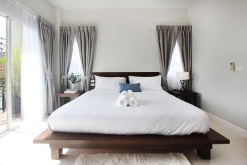 Spacious bedroom with large bed, bedside tables and lamps, and natural light from windows.