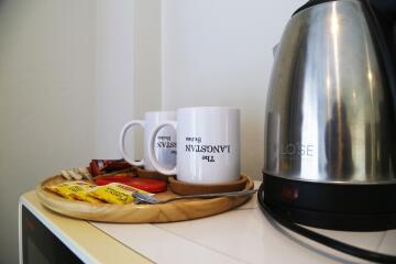 Coffee and tea setup with two mugs, an electric kettle, and snacks