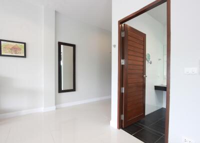 Modern interior with a white wall, a large mirror, and a door leading to a bathroom