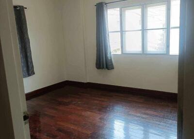 Empty bedroom with wooden floor, two windows with grey curtains