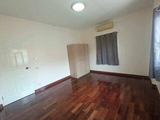 Spacious, empty bedroom with wooden floor, a wardrobe, air conditioning unit, and a window with curtains