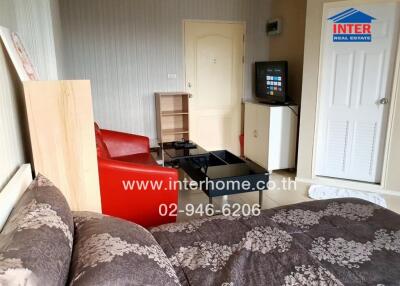Living room with a bed, red chairs, a TV on a cabinet, and a door