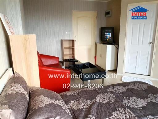 Living room with a bed, red chairs, a TV on a cabinet, and a door