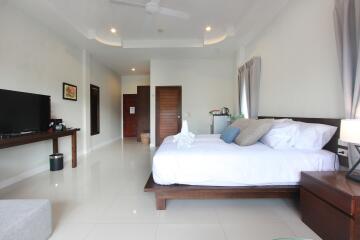 Spacious modern bedroom with white walls, double bed, ceiling fan, and a flat-screen TV.