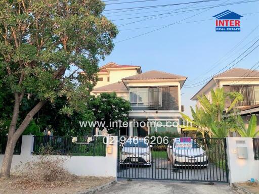 Exterior view of a multi-story house with a gated driveway, two parked cars, and trees on the premises