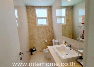Well-lit modern bathroom with large mirror, sink, toilet, and windows providing natural light.
