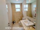 Well-lit modern bathroom with large mirror, sink, toilet, and windows providing natural light.