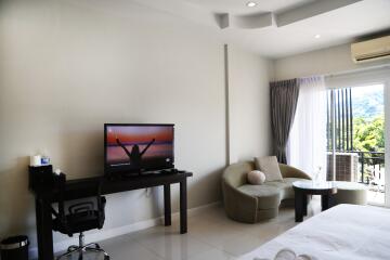 Modern bedroom with desk, TV, seating area, and a view to a balcony