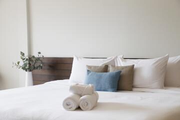 A neatly arranged bedroom with a made-up bed, accent pillows, and towels