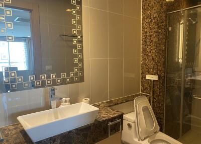 Modern bathroom with tiled walls, a mirror, sink, toilet, and a glass shower enclosure
