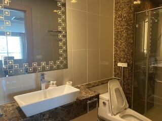 Modern bathroom with tiled walls, a mirror, sink, toilet, and a glass shower enclosure