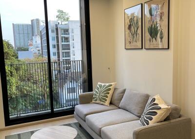Modern living room with a grey sofa, coffee table, and large window overlooking a cityscape.