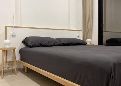 Minimalist bedroom with wooden bed frame and black bedding, including bedside tables and ambient lighting