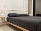 Minimalist bedroom with wooden bed frame and black bedding, including bedside tables and ambient lighting