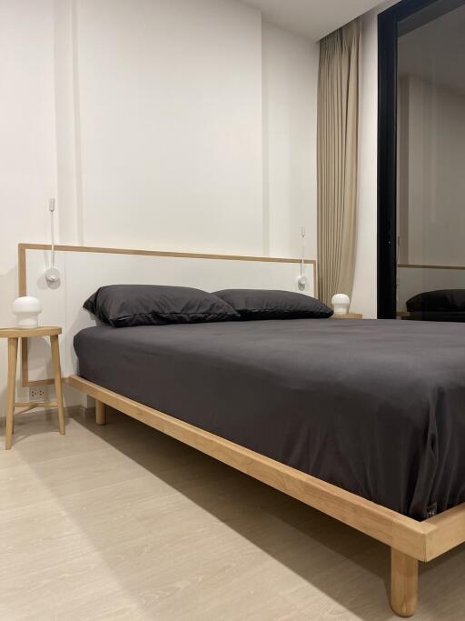 Minimalist bedroom with wooden bed frame and black bedding, including bedside tables and ambient lighting