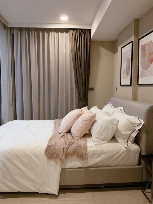 A modern, cozy bedroom with a neatly made bed, decorative pillows, and framed artwork.