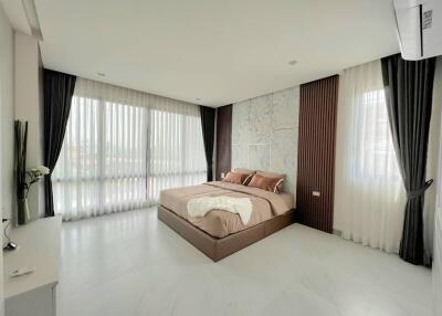 Spacious bedroom with large windows, modern decor, and a bed with brown bedding