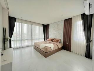 Spacious bedroom with large windows, modern decor, and a bed with brown bedding