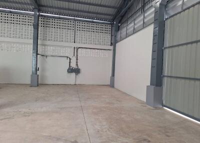 Empty interior of a spacious industrial building with concrete flooring and large metal doors.