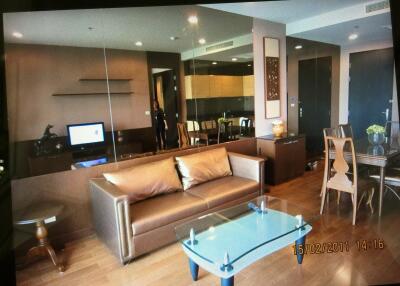 Modern living room with brown sofa, glass coffee table, dining area, and mirrored wall