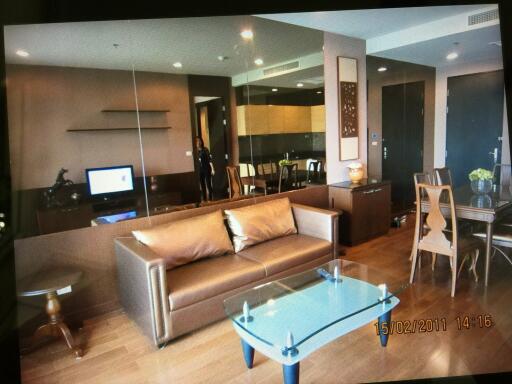 Modern living room with brown sofa, glass coffee table, dining area, and mirrored wall