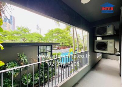 A balcony with views of a garden and city skyline, featuring two air conditioning units.
