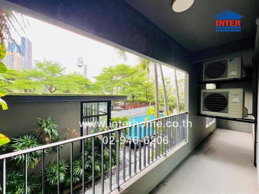 A balcony with views of a garden and city skyline, featuring two air conditioning units.