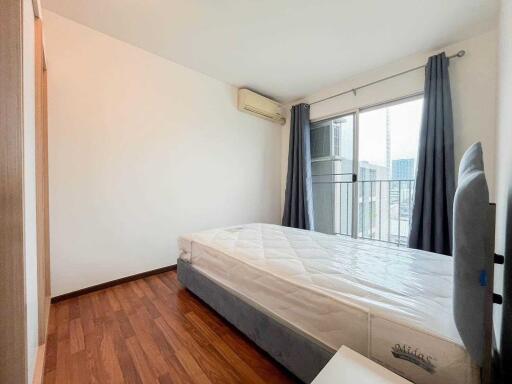 Spacious bedroom with a large bed, wooden flooring, air conditioning, and a window with curtains.