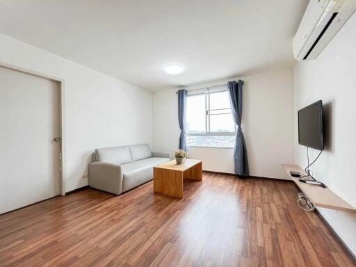 Modern living room with a sofa, coffee table, wall-mounted TV, and window with curtains