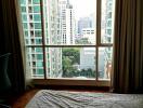 Bedroom with large window and view of modern city buildings