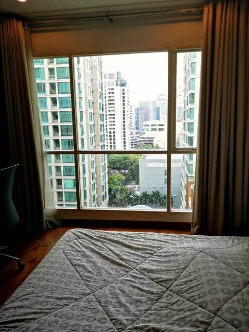 Bedroom with large window and view of modern city buildings