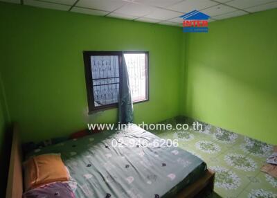 A bedroom with bright green walls, a bed, window with bars, tiled floor, and part of a wooden piece of furniture.