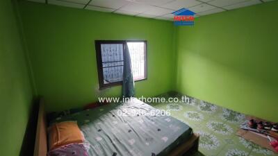 A bedroom with bright green walls, a bed, window with bars, tiled floor, and part of a wooden piece of furniture.