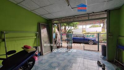 Photo of a cluttered indoor space with a green wall, tiled floor, a blue car parked outside, and various items including a scooter and household tools