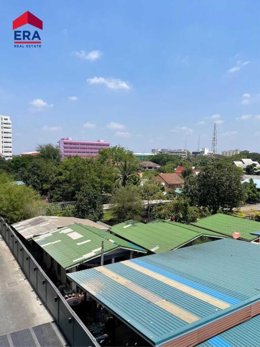 Rooftop view of nearby buildings and greenery with a blue sky