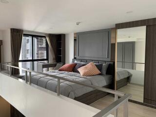 Modern bedroom with glass railings, large window with curtains, and decorative pillows