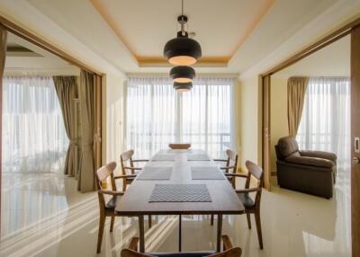 Modern dining area with wooden table and chairs, pendant lighting, and large windows