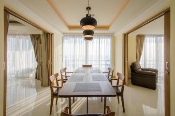 Modern dining area with wooden table and chairs, pendant lighting, and large windows